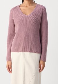 Maglione a V, con maniche lunghe in morbida texture a coste, di colore lavanda. Abbinato a una gonna color crema con design asimmetrico.