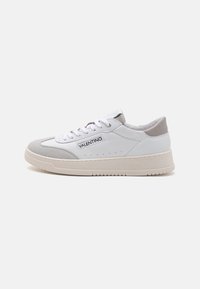 Hvide sneakers med en kombination af læder og ruskind, med en grå akcent ved hælen, flade snørebånd og en tekstureret beige gummisål.