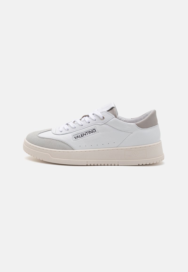 Hvide sneakers med en kombination af læder og ruskind, med en grå akcent ved hælen, flade snørebånd og en tekstureret beige gummisål.