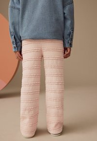 Rosa strukturierte Hose mit horizontalem Streifenmuster und Spitzenbesatz; kombiniert mit einer hellen Jeansjacke, Rückansicht gezeigt.