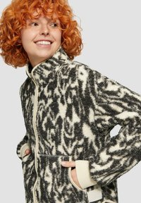 Fleece jas met een zwart-wit abstract patroon, hoge kraag, ritssluiting en voorzakken met ribbenboorden en crèmekleurige accenten.