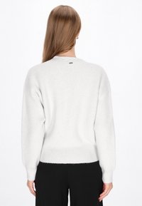 Fehér, textúrált pulóver laza szabású, bordás mandzsettákkal és derékrésszel. Kicsi, márkázott címkével rendelkezik a nyakán.