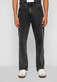Jean en denim noir avec une finition délavée, coupe droite, design à cinq poches et surpiqûres contrastantes. Assortis à des baskets blanches et beige.