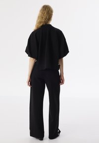 Zwarte oversized sweatshirt met korte mouwen en een losse pasvorm, gecombineerd met zwarte wijde broek. Vlakke textuur met minimale details.