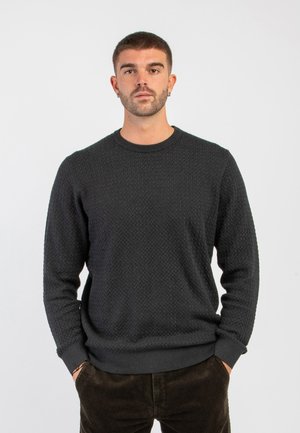 Maglione grigio scuro in lavorazione a maglia strutturata, con collo girocollo e polsini e orlo a coste, indossato da un modello con le mani in tasca, su uno sfondo bianco.