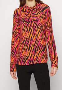 Langarmshirt met een opvallend oranje en roze tijgerstrepenpatroon op een zwarte achtergrond. Inclusief een striksluiting en knoopsluiting.