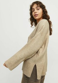 Ljus beige tröja med avslappnad passform, ribbad nederkant och sidofickor. Tillverkad av mjukt material med en subtil texturerad finish.