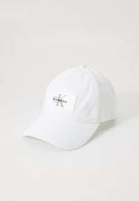 Witte baseballpet met een gebogen rand, stoftextuur, met een rechthoekig label waarop "Calvin Klein" en een gestileerd logo is afgebeeld.
