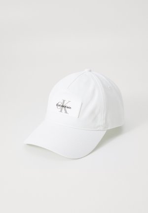 Witte baseballpet met een gebogen rand, stoftextuur, met een rechthoekig label waarop "Calvin Klein" en een gestileerd logo is afgebeeld.