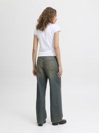 Camiseta branca de manga curta combinada com uns jeans azuis claros, largos e desbotados. Os jeans têm um corte reto e bolsos traseiros. Botas pretas até ao tornozelo.