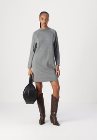 Vestido de moletom cinza com mangas longas, corte descontraído e fendas laterais, acompanhado de botas de cowboy de couro castanho e uma bolsa redonda preta.