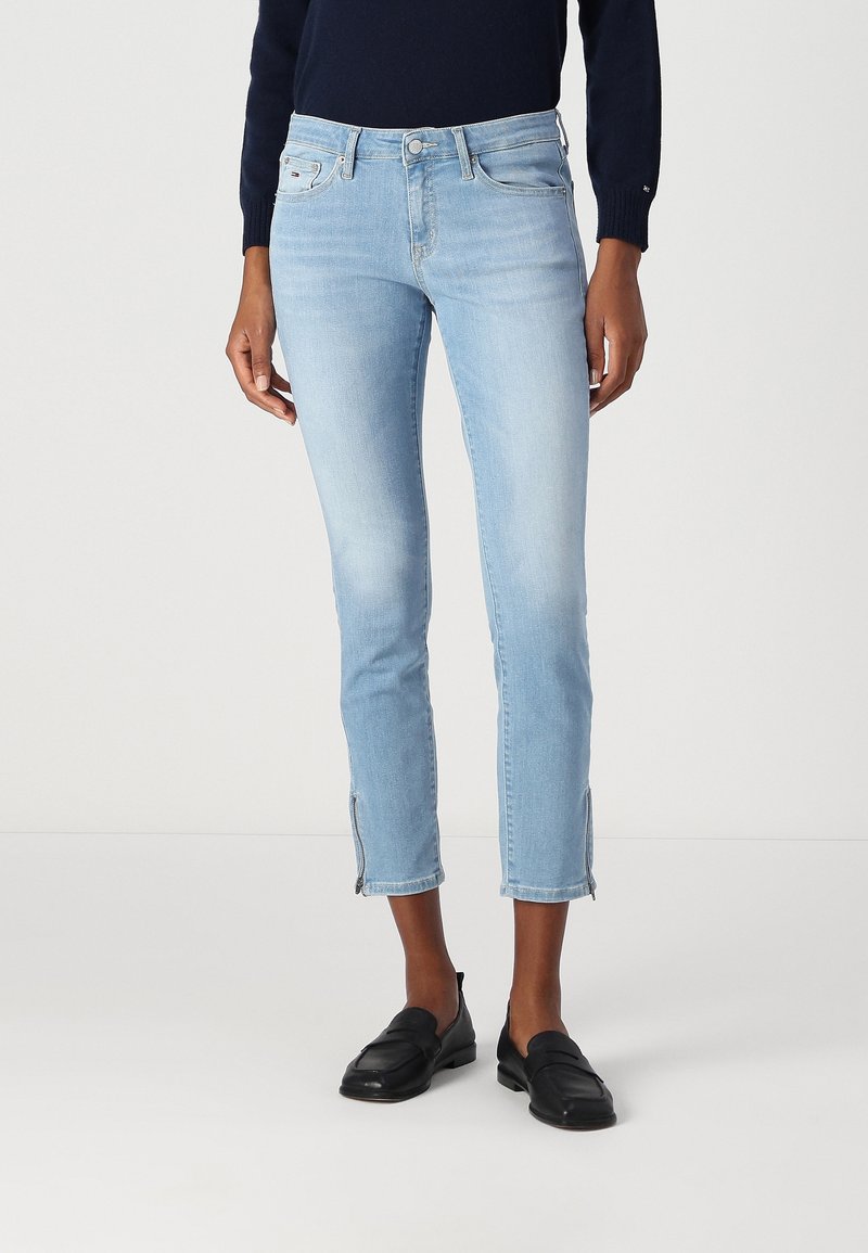 Jeans recortados de color azul claro en denim desgastado con un corte ajustado, cremalleras laterales en el dobladillo y un diseño clásico de cinco bolsillos.