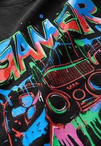 Schwarzer Kapuzenpullover mit lebhaftem "GAMER"-Text in Blau, Rot und Grün, verziert mit verspielten Spritzmustern und Grafiken von Gaming-Controllern.
