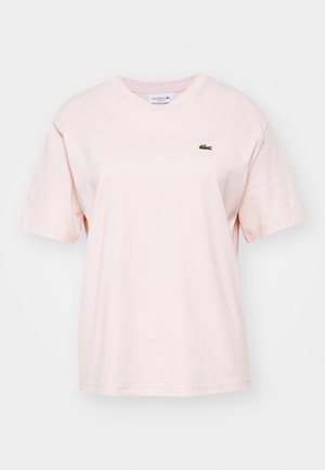 Jasnoróżowa bawełniana koszulka z krótkim rękawem, okrągłym dekoltem i małym zielonym logo Lacoste na lewej piersi. Miękka tekstura, luźny krój.