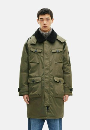 Olijfgroene parka met zwarte faux shearling kraag, meerdere frontzakken en knoopsluitingen, gemaakt van een glad, waterafstotend materiaal.