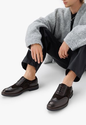 Donkerbruine oxford schoenen met brogue details, gemaakt van leer en suede, platte zolen en ronde neus. Gekocht in combinatie met zwarte broeken.