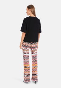 Black short-sleeve top with a straight hem paired with multicolored zigzag patterned pants in shades of pink, orange, and black.