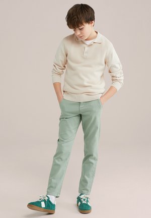 Polo en tricot beige clair avec col et texture côtelée, associé à un pantalon slim fit vert menthe et des baskets vertes avec accents blancs.