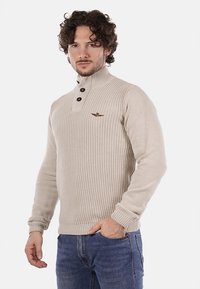 Maglione beige lavorato a maglia con colletto alto, dotato di tre bottoni neri, polsini a coste e un piccolo logo marrone sul petto.