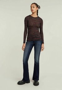 Haut à manches longues à motif camouflage dans des tons rouge foncé et noir, associé à un jean évasé bleu marine et des bottes plateforme noires imposantes.