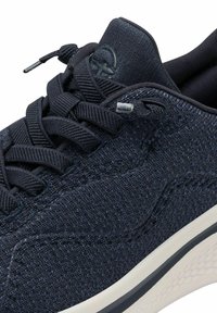 Marineblaue Sneaker mit strukturiertem Obermaterial, traditioneller Schnürung und weißer Gummisohle. Kleines Logo an der Seite, minimalistisches Design.