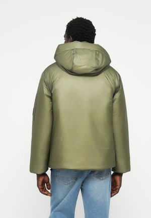 Padded jacket in olive green with a hood, featuring a smooth texture, dropped shoulders, and a zippered pocket on the left arm.