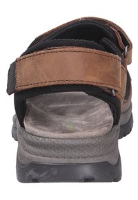 Brown leather sandal with black textile straps, adjustable Velcro closure, cushioned grey footbed, and textured black rubber sole.