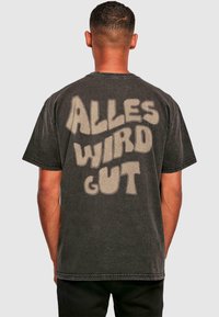 Sort bomulds t-shirt med stort, lyse teksttryk på ryggen, der står "ALLES WIRD GUT." Korte ærmer og løs pasform.