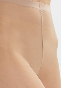 Beige, semi-transparente Strumpfhosen mit glatter Textur und elastischem Bund. Verfügt über eine Mittelnaht und nahtloses Design für zusätzlichen Komfort.