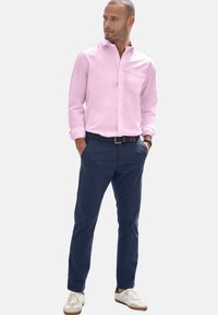 Lichtroze button-up shirt met een borstzak, marineblauwe chinos en witte sneakers. Het shirt heeft opgerolde mouwen; een casual outfitstructuur.