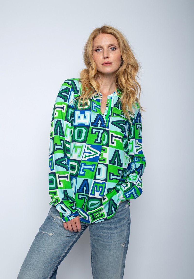 Zielono-niebieska bluzka z długim rękawem i dekoltem w kształcie litery V, z geometrycznym wzorem liter i kształtów. Lekki materiał i luźny krój.