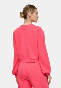 Felpa cropped rosa con maniche lunghe, polsini a costine e collo rotondo. Realizzata in tessuto morbido, presenta una superficie liscia e un design minimale.
