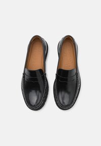 Mocassins en cuir noir avec une finition polie, présentant un design cousu et une semelle intérieure rembourrée marron ; style à enfiler sans matériel visible.