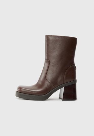 Brown leather ankle boot with a rounded toe, smooth texture, and a chunky wooden heel. Side seam detail and subtle sheen.