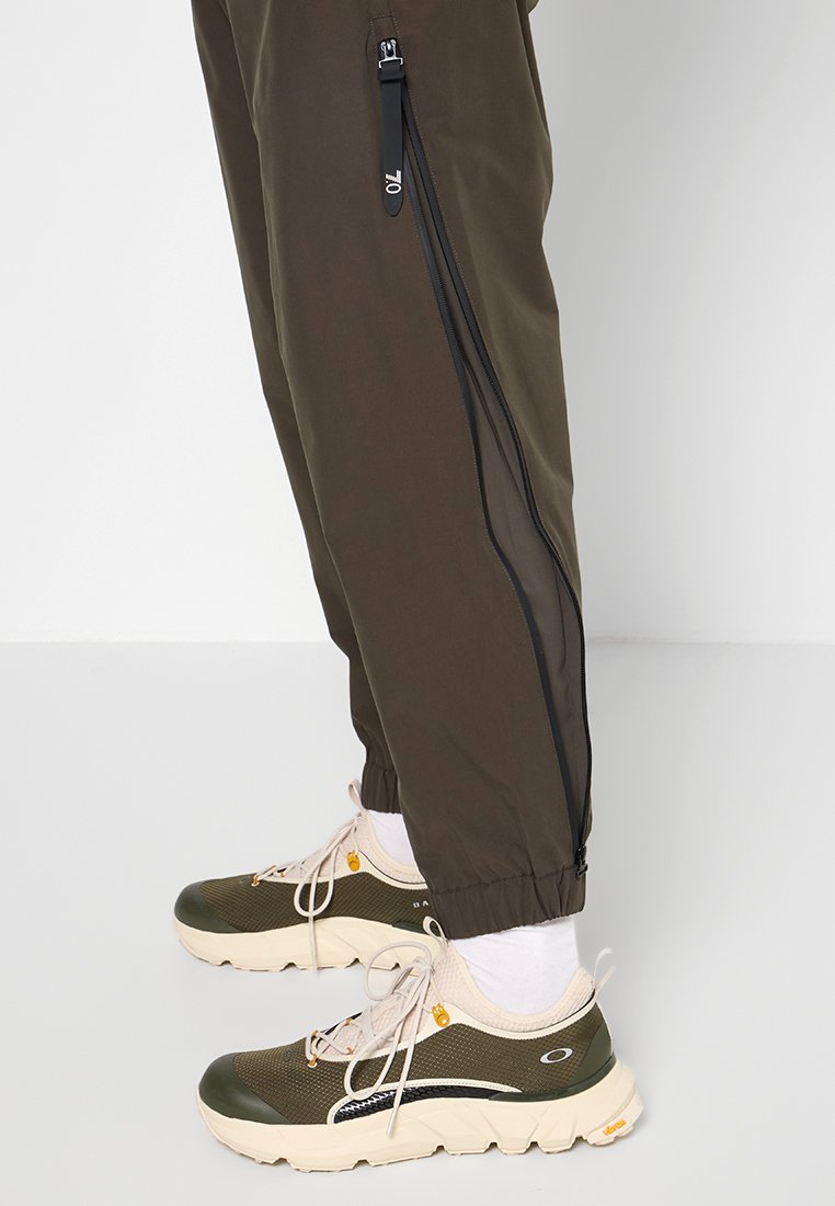 Pantaloni verde oliva con zip laterali, polsini elasticizzati e texture liscia, abbinati a sneakers beige chiaro e verdi con design con lacci.