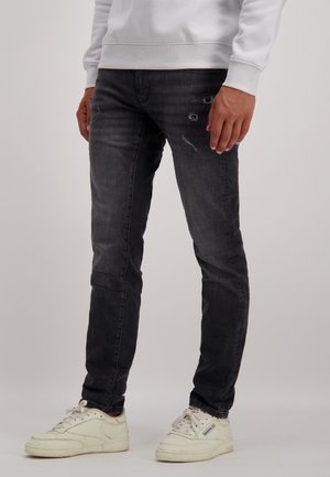 Slim-fit, donkergrijze jeans met versleten details en subtiele vervaging. Gecombineerd met witte sneakers met een simpel ontwerp.