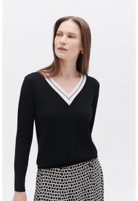 Maglione nero a V con bordi bianchi e grigi a contrasto, caratterizzato da maniche lunghe e una forma aderente, abbinato a pantaloni con fantasia.
