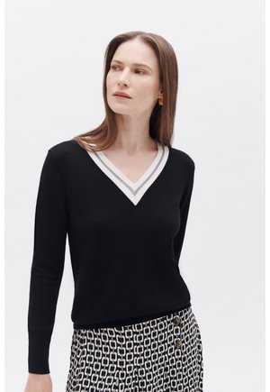 Maglione nero a V con bordi bianchi e grigi a contrasto, caratterizzato da maniche lunghe e una forma aderente, abbinato a pantaloni con fantasia.