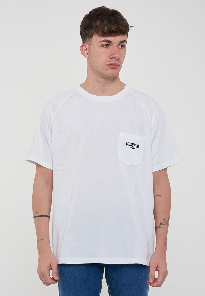 T-shirt di cotone bianco con scollatura rotonda, maniche raglan corte e taschino sul petto con il testo nero "MOSCHINO."