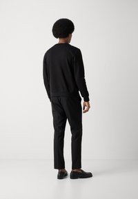 Sudadera negra con cuello redondo y mangas largas, combinada con pantalones negros. El modelo lleva zapatos negros con un diseño texturizado.