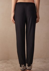 Zwarte pyjamabroek met een elastische tailleband, voorzien van kantaccenten bij de uiteinden en gemaakt van een gladde, lichte stof.