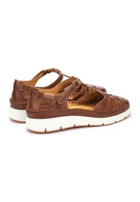 Sandalias de cuero marrón con diseño abierto, acentos trenzados y correa ajustable. Suela de goma blanca con detalle de costura marrón.