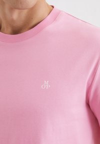 Šviesiai rožinė trumpas rankoves su apvaliu iškirpimu marškinėliai, pagaminti iš medvilnės, su mažuoju baltu „M O' P“ logotipu ant krūtinės. Lygus paviršius.