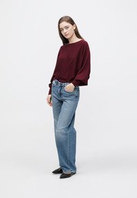 Suéter largo de cor vinho, jeans de cintura alta azuis, sapatos pretos com bico pontiagudo. Textura suave, design descontraído, ajuste casual e moderno.