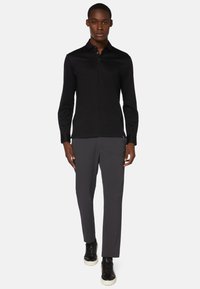 Zwarte lange mouwen polo met een kraag en knoopsluiting, gecombineerd met grijze broeken en zwarte sneakers met een witte zool.