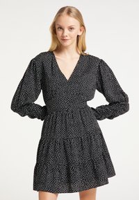 Rochie neagră cu modele albe sub formă de inimă, decolteu adânc în V, mâneci lungi bufante și fustă cu volanuri în straturi. Fabricată dintr-un material ușor.