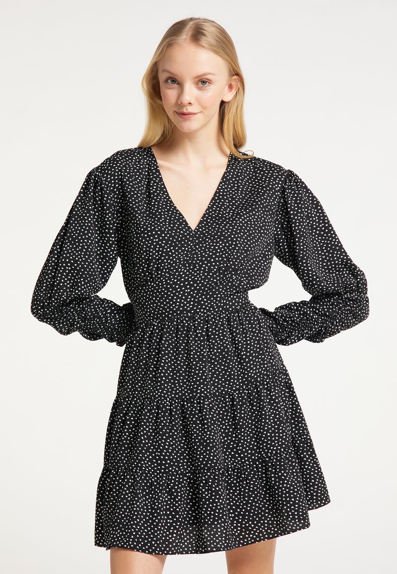 Rochie neagră cu modele albe sub formă de inimă, decolteu adânc în V, mâneci lungi bufante și fustă cu volanuri în straturi. Fabricată dintr-un material ușor.