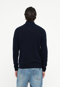 Pulover tricotat de culoare bleumarin, cu guler înalt, tiv cu benzi și mâneci lungi. Material texturat cu detalii verticale în cabluri.