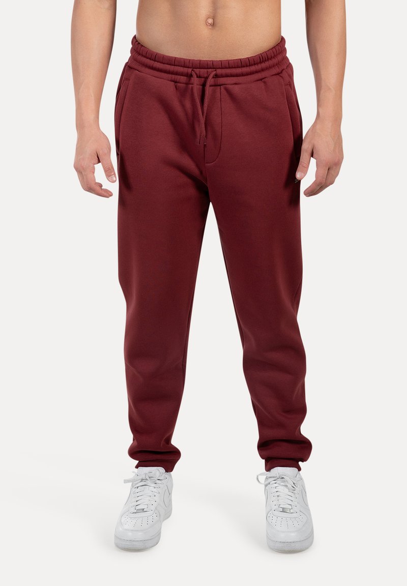 Maroons joggerbukser med elastisk talje, sidelommer og manchetter ved anklerne, parret med hvide sneakers. Glat stofstruktur.