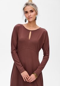 Robe marron à manches longues avec un col rond et une ouverture en forme de trou de serrure. Tissu doux, corsage ajusté, jupe évasée, et détails de couture visibles.